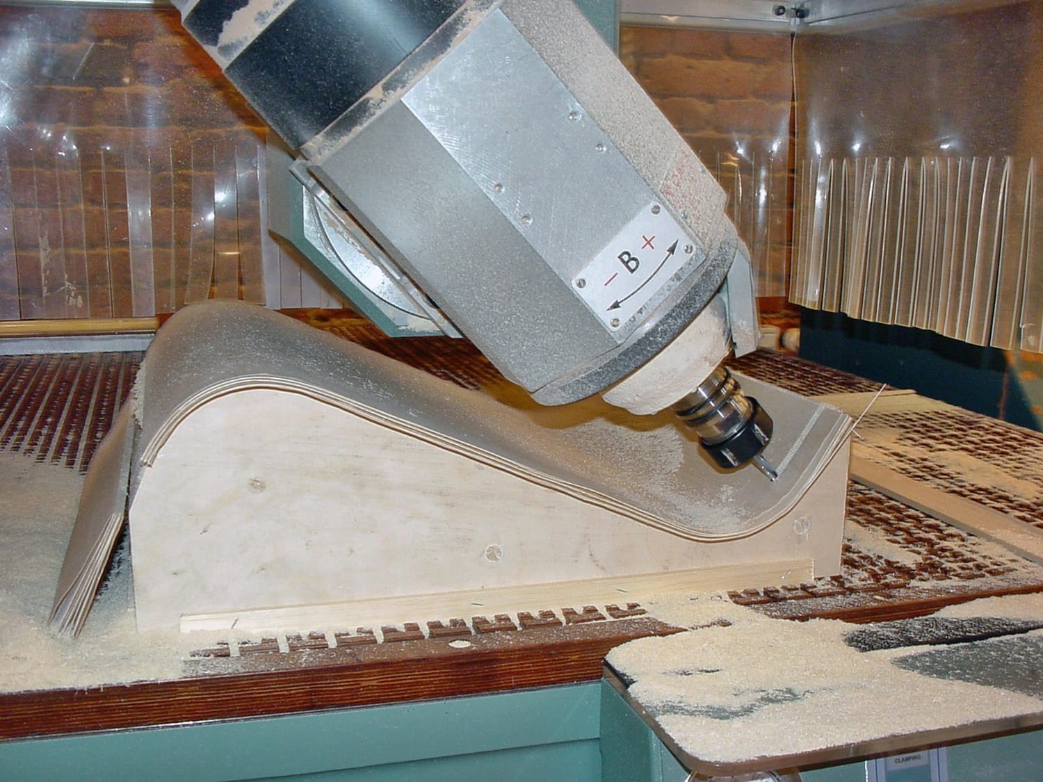 Kuvassa cnc-kone työstää kaarevia muotoja sisältävässä muotissa olevaa vanerikappaletta.