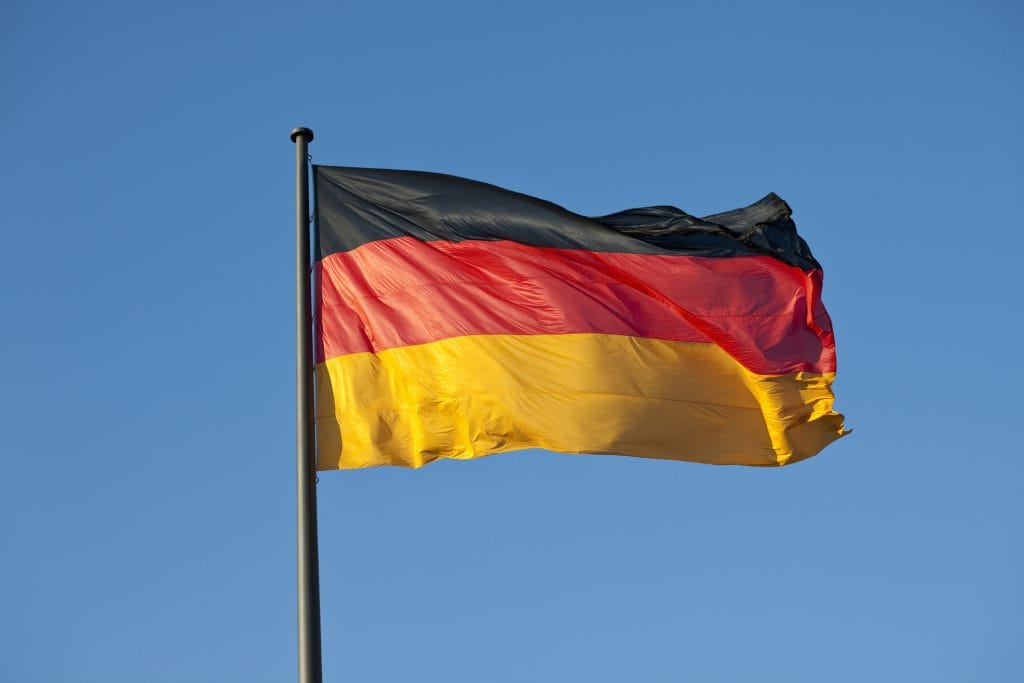 Liehuva Saksan lippu lipputangossa sinistä taivasta vasten.