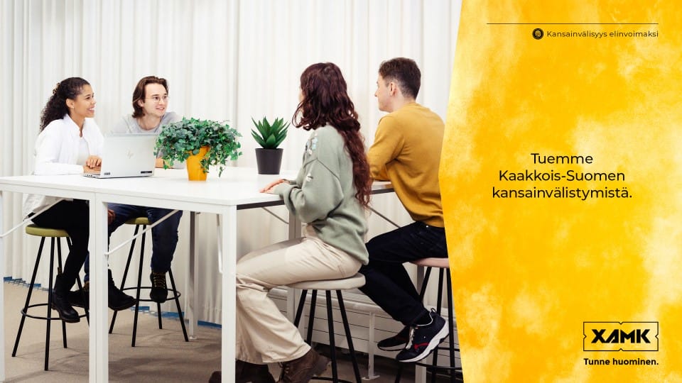 Neljä opiskelijaa istuu pöydän ympärillä. Rinnalla teksti "Tuemme Kaakkois-Suomen kansainvälistymistä".