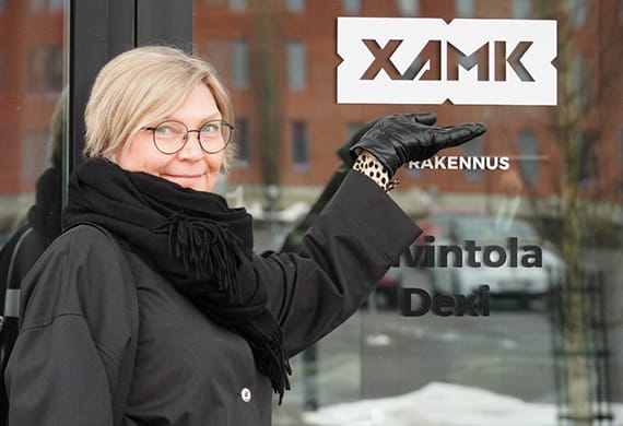 Nainen osoitta ovessa näkyvää Xamk-logoa.