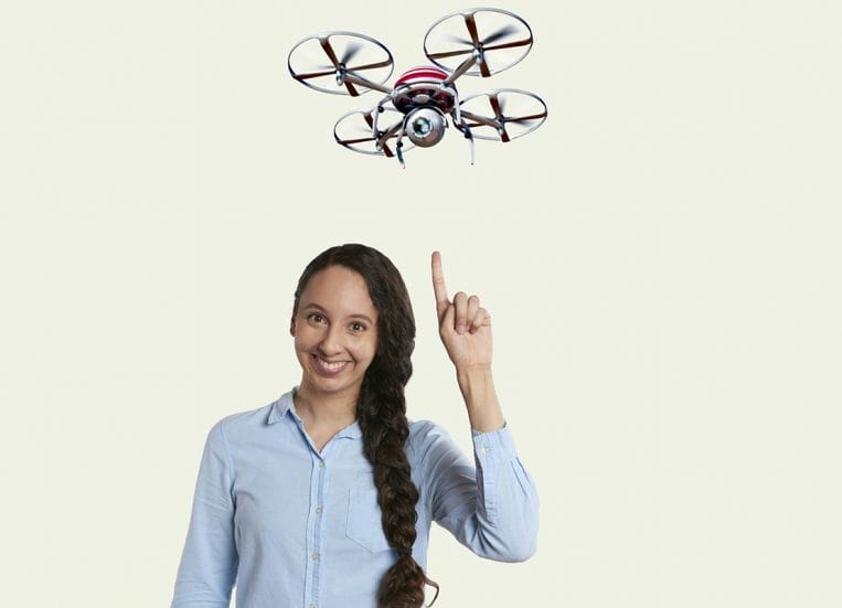 Nainen osoittaa päänsä yläpuolella lentävää dronea.