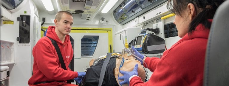 Mies ja nainen harjoittelevat hoitotoimenpidettä ambulanssisimulaattorin sisällä.