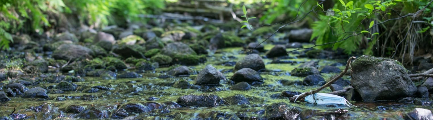 kuva luonnosta ja purosta jossa on roskana hengityskasvomaski
