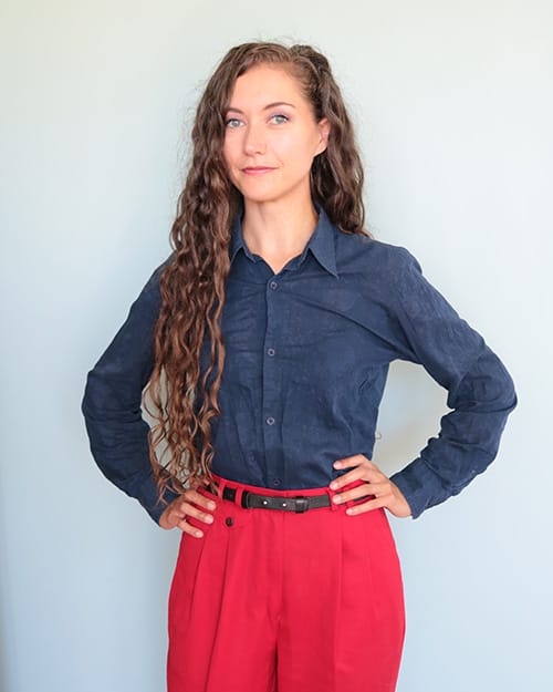 Heli Salomaa: pitkähiuksinen nainen poseeraa sinisessä kauluspaidassa ja punaisissa housuissa.