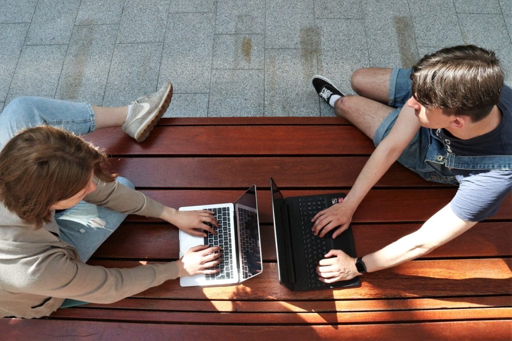 Photo. Two persons working together with laptops in campus atmosphere.