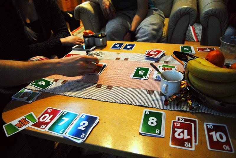 Photo. Persons around the table. Playing cards, bananas and coffee mug on the table.