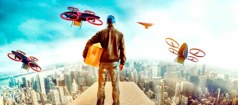 Henkilö seisoo kaupungin yllä kainalossaan paketti. Hänen ympärillään lentää droneja, jotka myös kannattelevat paketteja.
