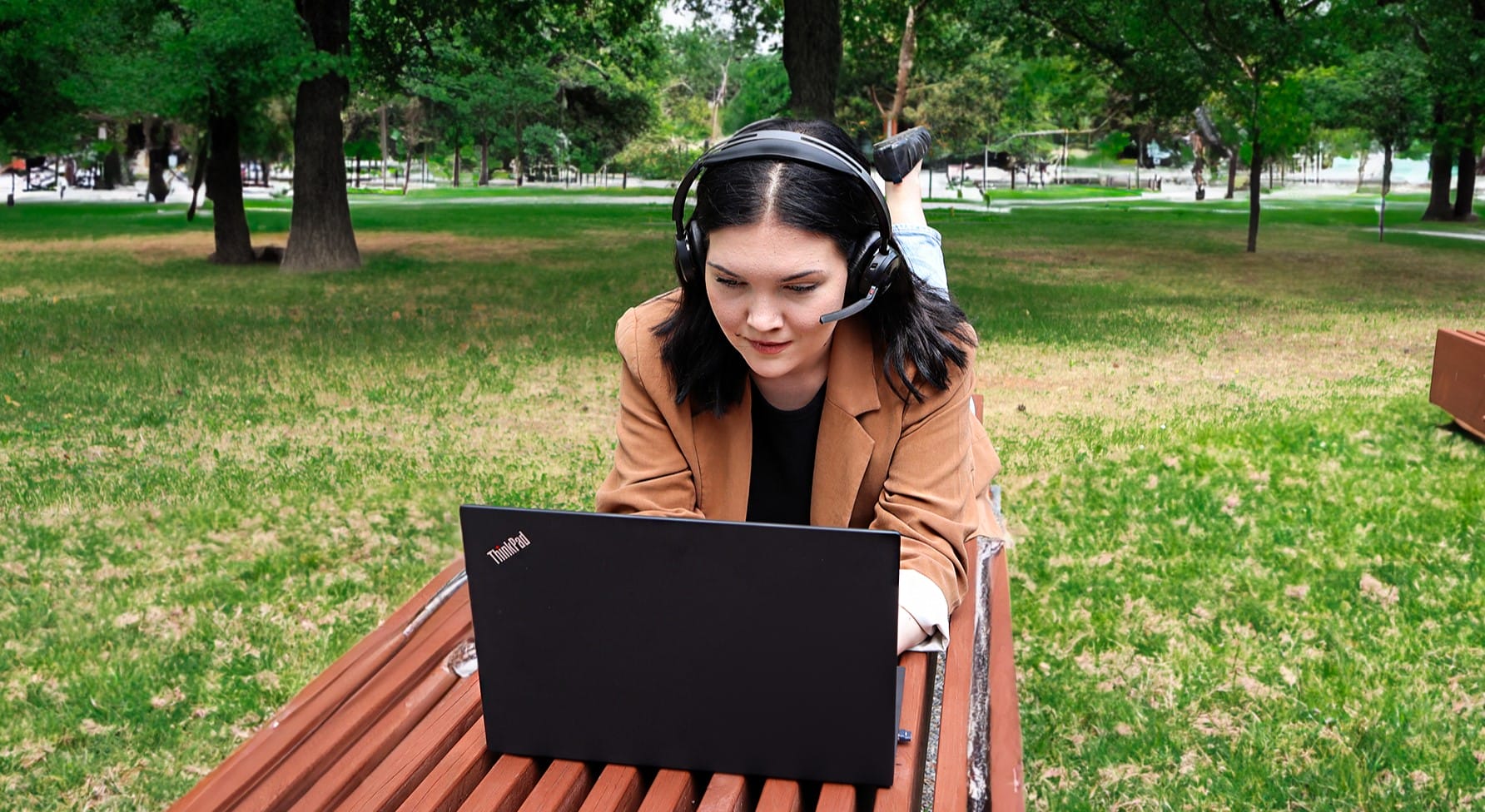 Nainen opiskelee puiston penkillä kannettavalla tietokoneella.