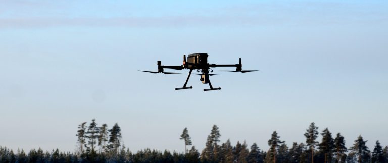 Miehittämätön ilma-alus eli drone lentää puiden latvojen yllä.