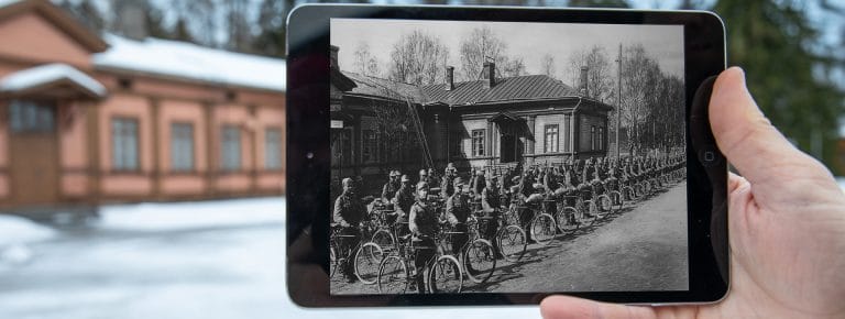 Vanhaa mustavalkoista valokuvaa tabletilla verrataan nykyisyyteen valokuvan ottopaikalla.