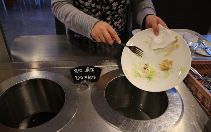 Henkilö kaapii lautaselta ruoantähteitä biojäteastiaan.