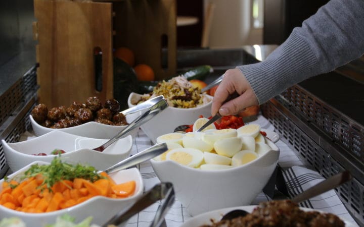 Henkilö nostaa lautaselleen salaattia pöydästä, jossa on tarjolla useaa erilaista tuoresalaattia.